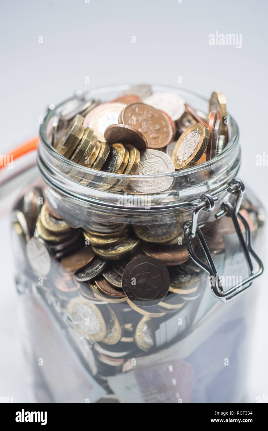 Savings UK - a glass storage jar completely full of british coins and notes, saved up.  Concept illustration for pension planning, rainy day fund, emergency money, home banking, cash in hand, accumulated wealth Stock Photo