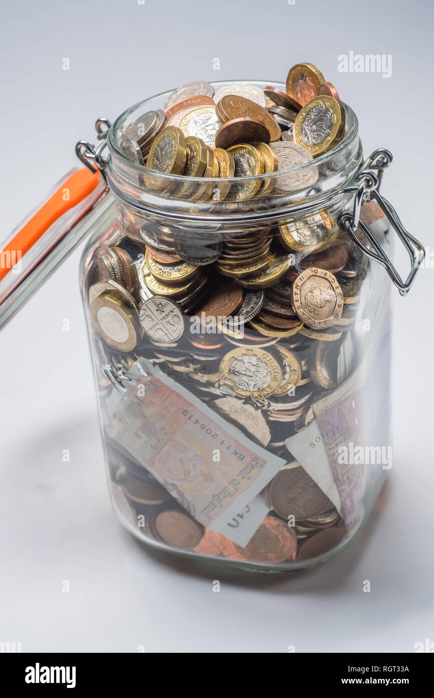 Savings UK - a glass storage jar completely full of british coins and notes, saved up.  Concept illustration for pension planning, rainy day fund, emergency money, home banking, cash in hand, accumulated wealth Stock Photo