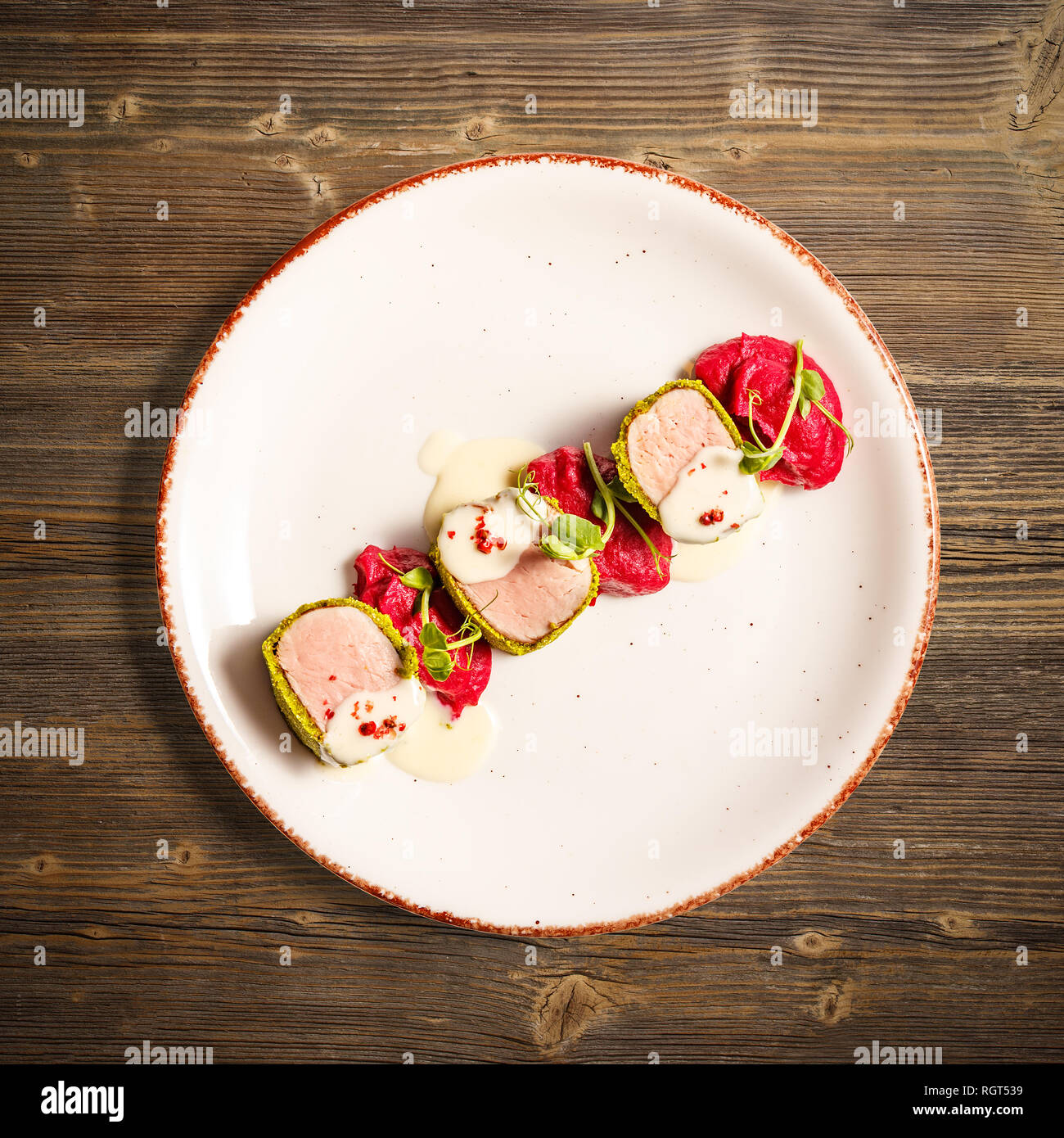 Flat lay of green crusted pork loin, mashed potatoes with beetroot and cheese sauce on wooden background Stock Photo