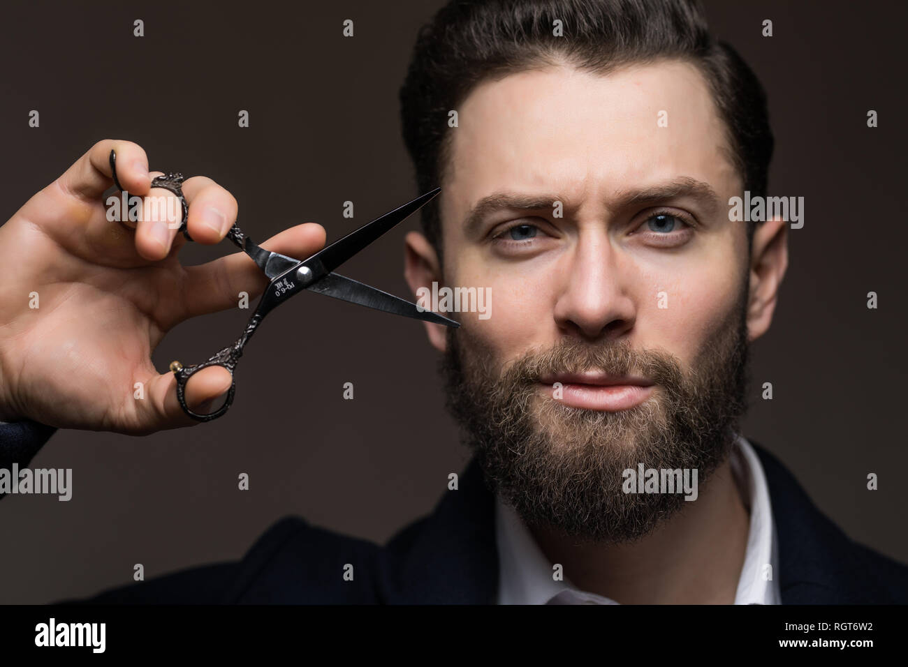 Portrait of stylish man with beard holding scissors near face. Barber