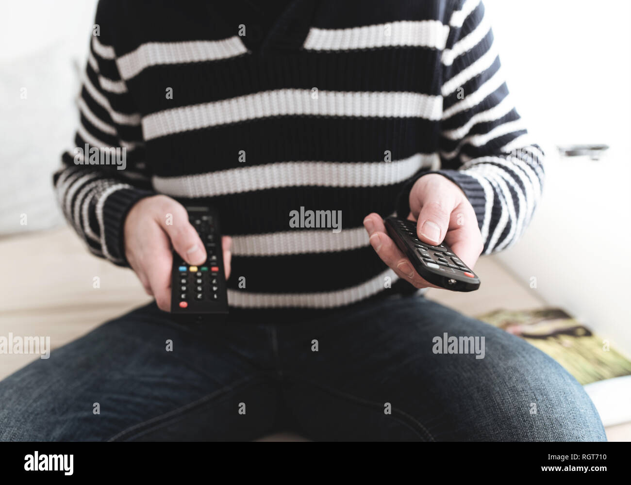 man sitting on sofa holding remote control in each hand Stock Photo