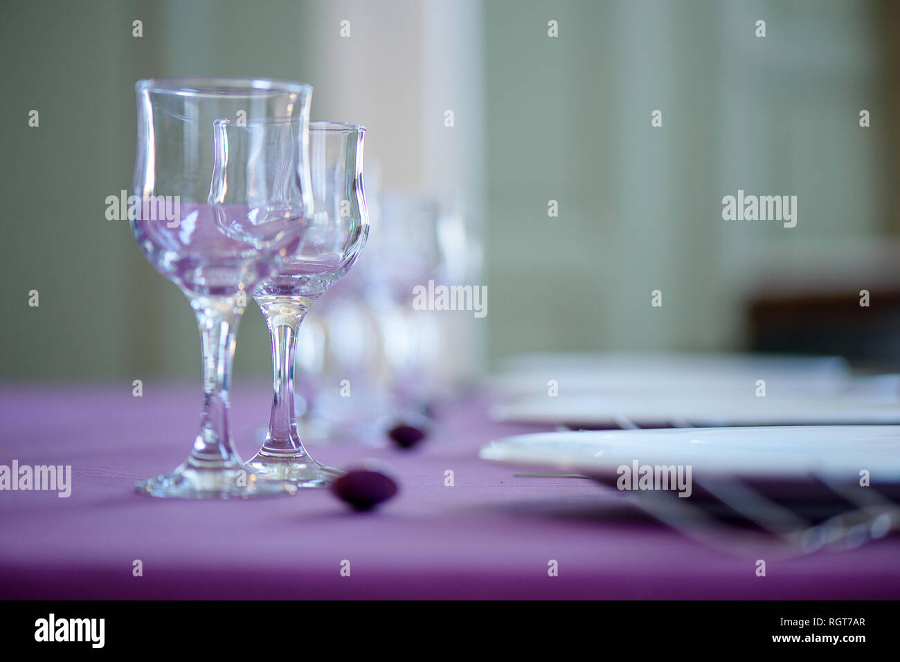 Clean table setting for fine dining with striking, elegant purple table cloth and focus on two crystal glasses for water and wine and white china Stock Photo