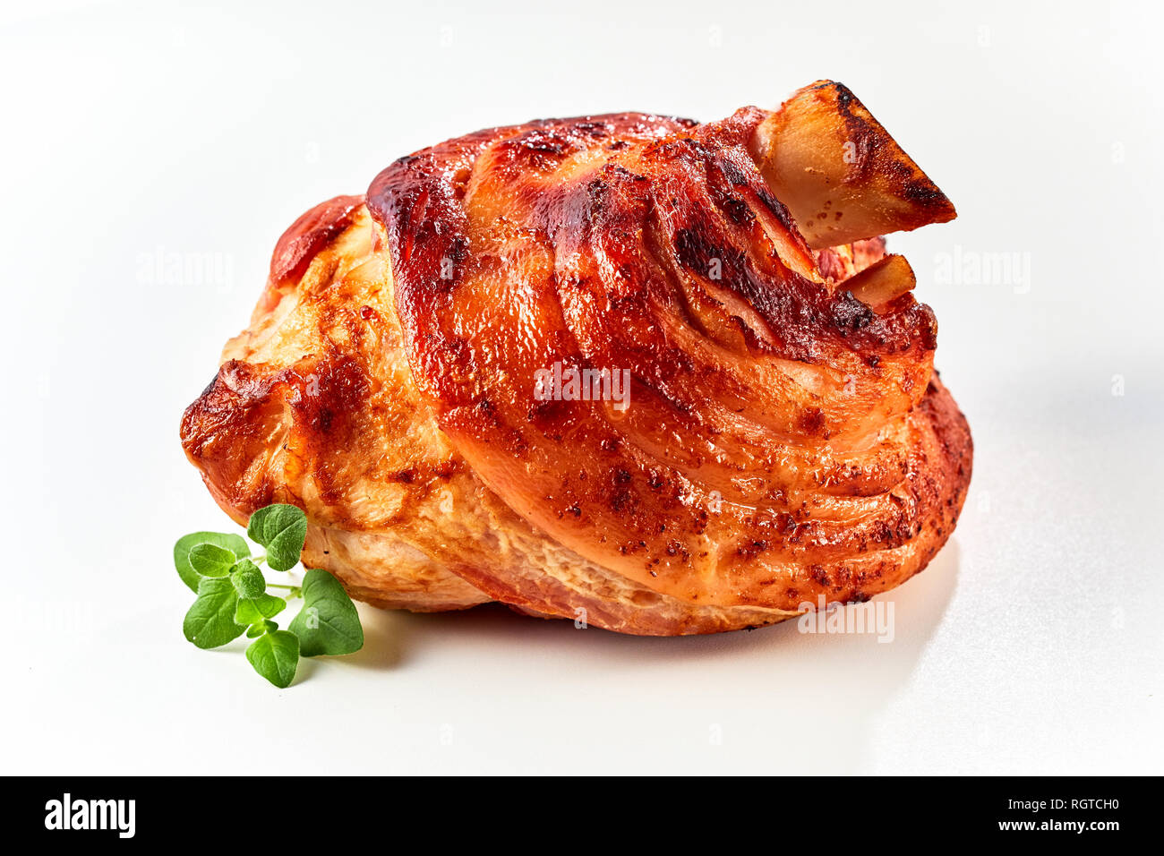 A crispy, golden roasted pork knuckle with a fresh herb garnish on a white background with copy space. Stock Photo