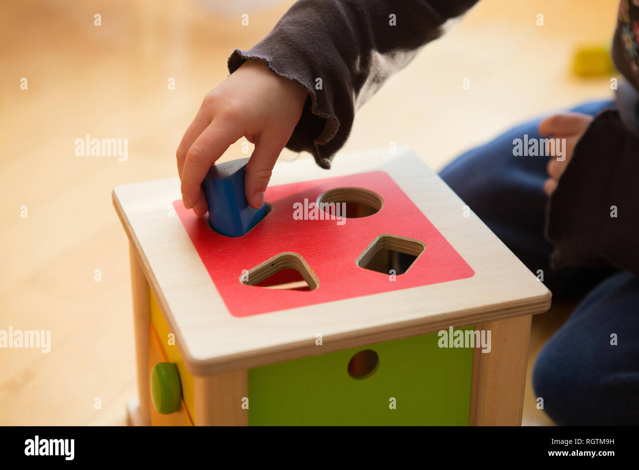 Child playing with wooden bricks in diffrent shapes and colors trying to put them into the proper hole Stock Photo