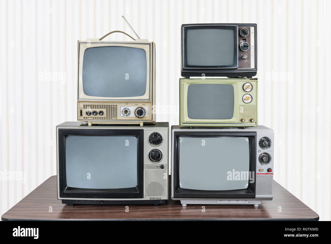 Five vintage televisions stacked on old wood table. Stock Photo