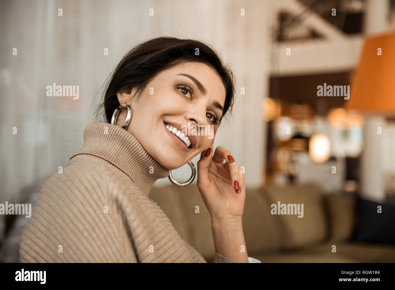 Appealing beaming lady with dark hair thoughtfully sitting on couch Stock Photo