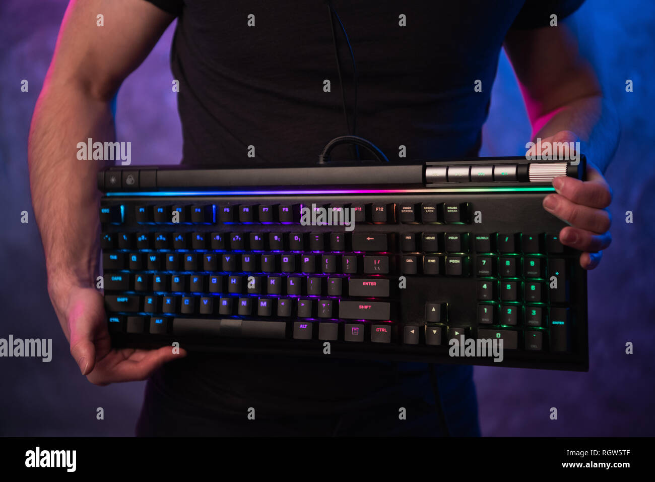 Close-up on gamer's hands holding a keyboard. Background is lit with neon lights Stock Photo