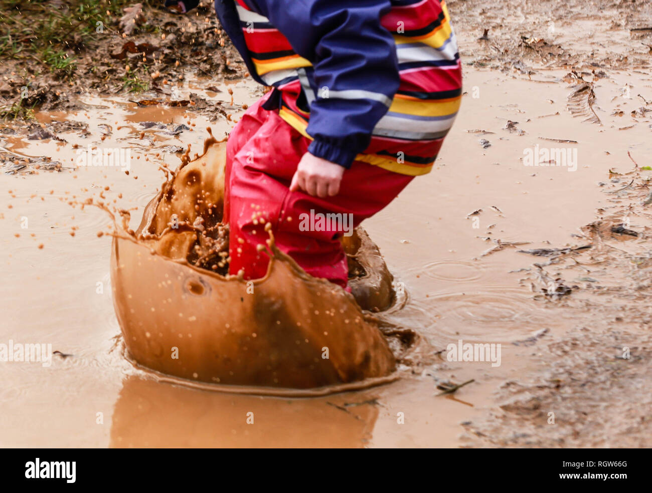 Young child playing in muddy puddle in wellies Stock Photo