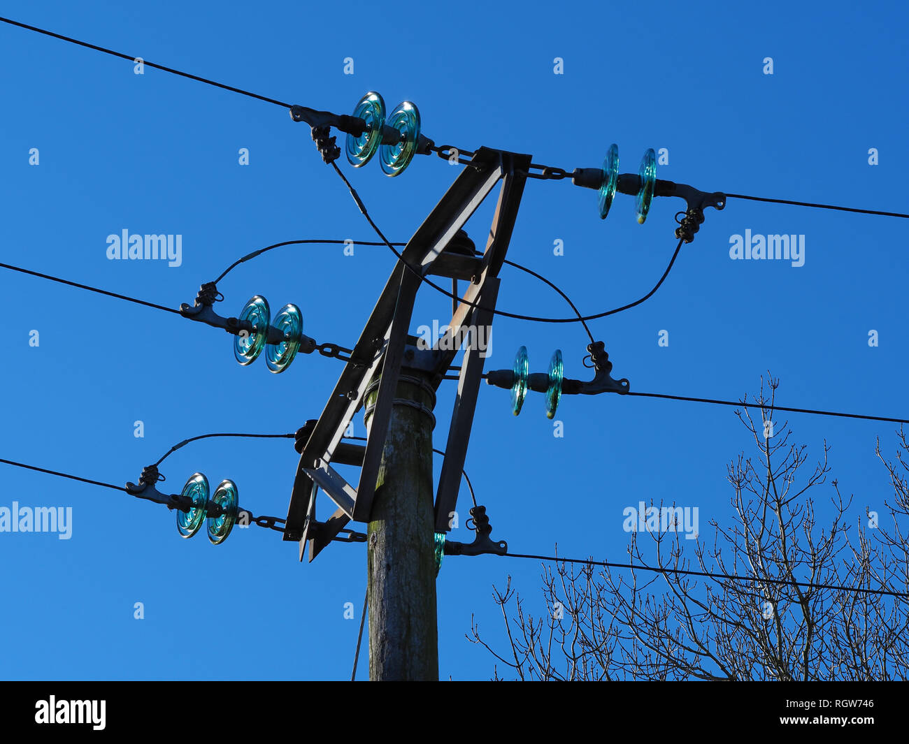 Overhead electric power lines with blue glass insulator disks and a clear blue sky Stock Photo