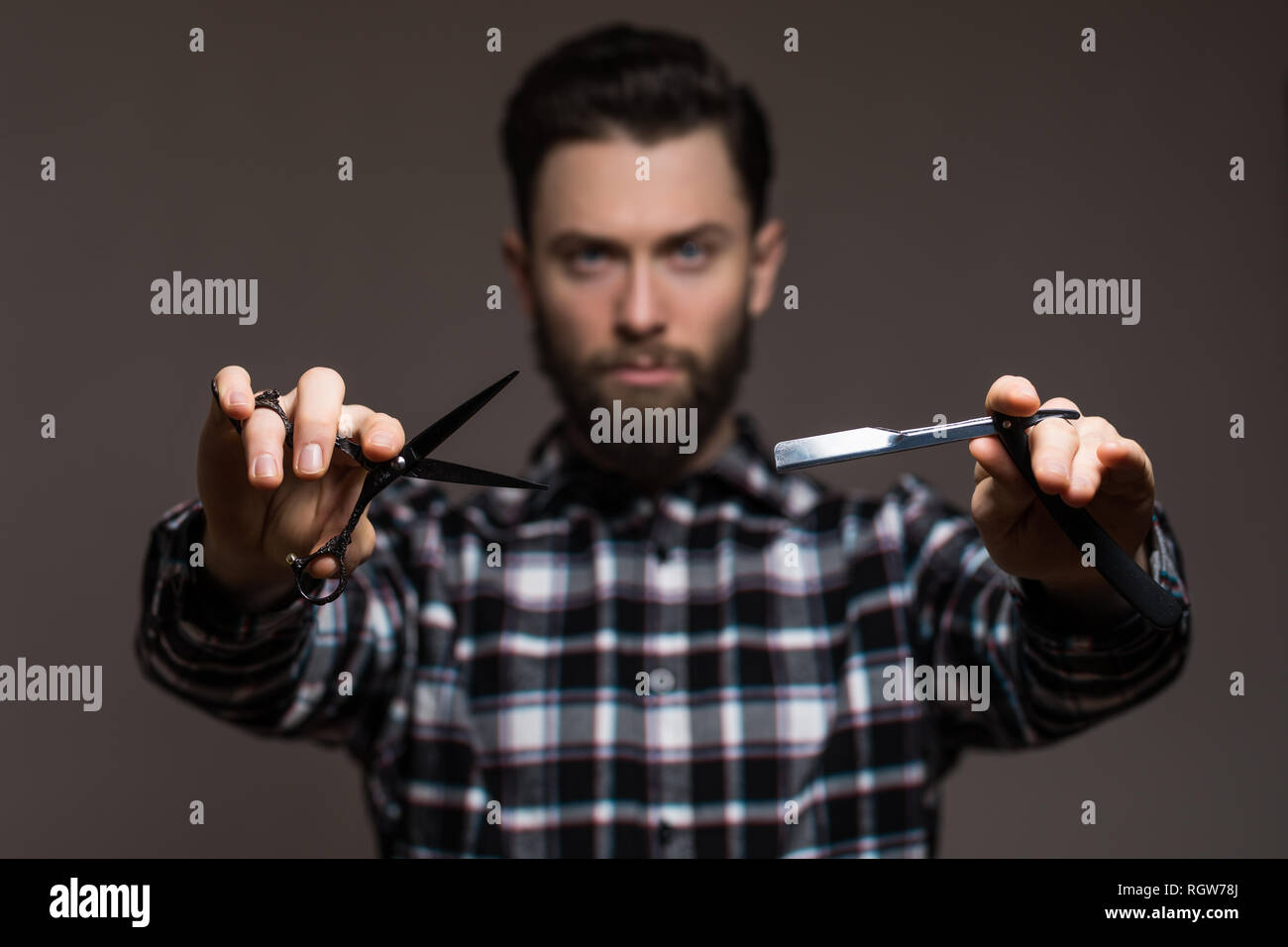 Young handsome man hairdresser or barber with beard dressed in plaid shirt demonstrating sharp