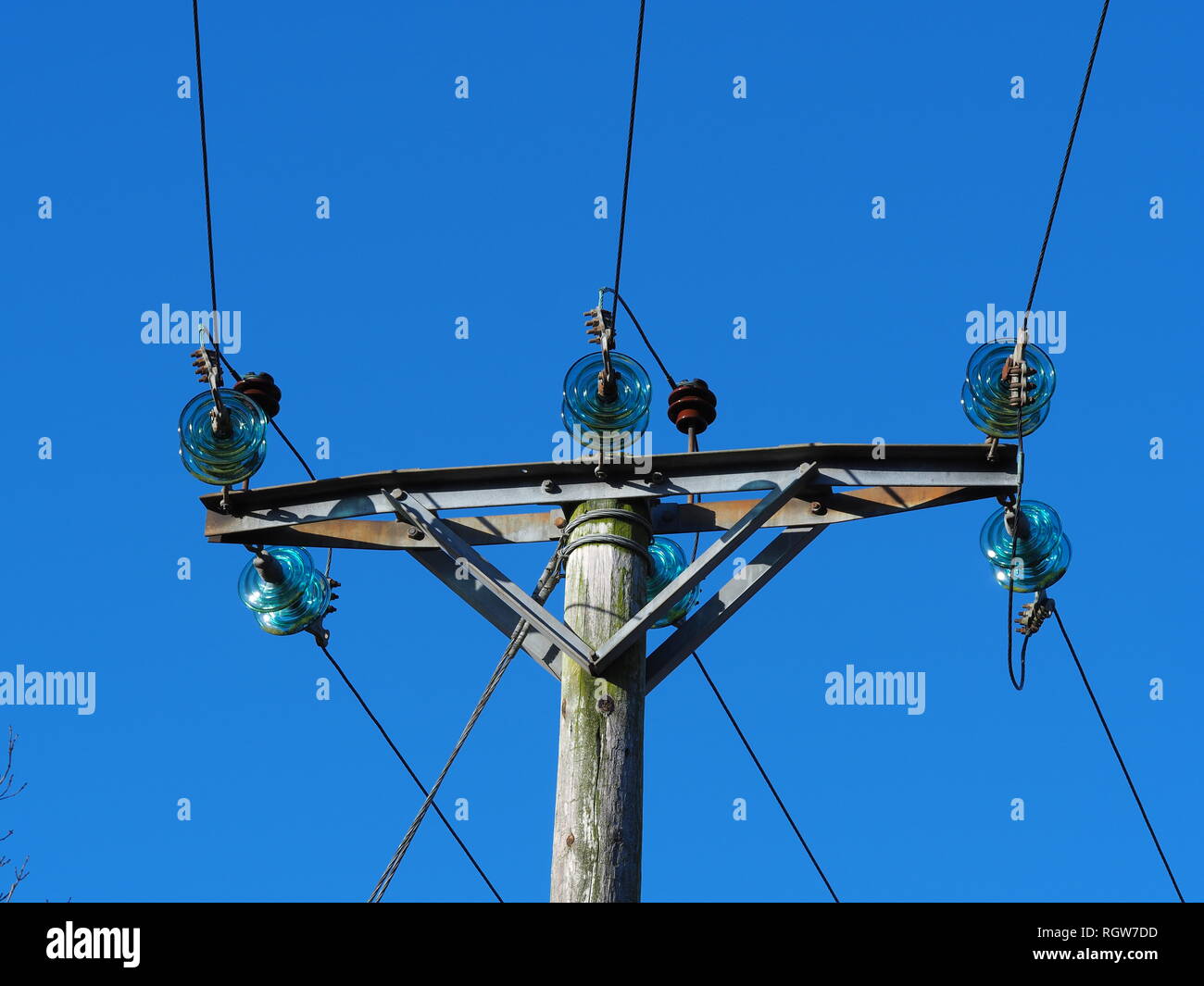 Overhead electric power transmission lines with blue glass insulators and a clear blue sky background Stock Photo