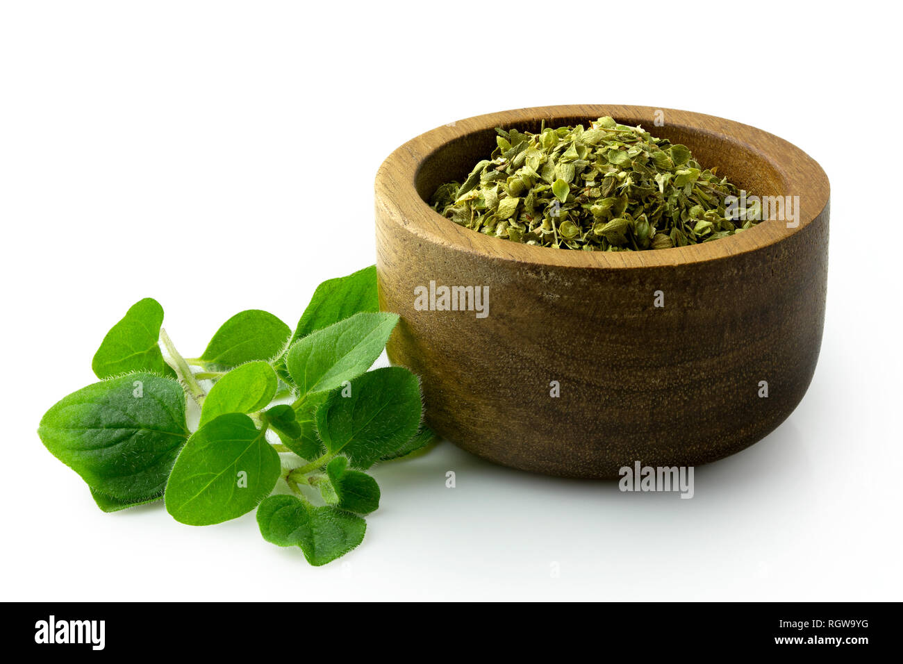 Dried chopped oregano in dark wood bowl next to fresh oregano leaves