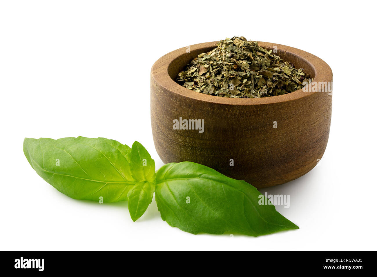 Dried chopped basil in a dark wood bowl next to fresh basil leaves