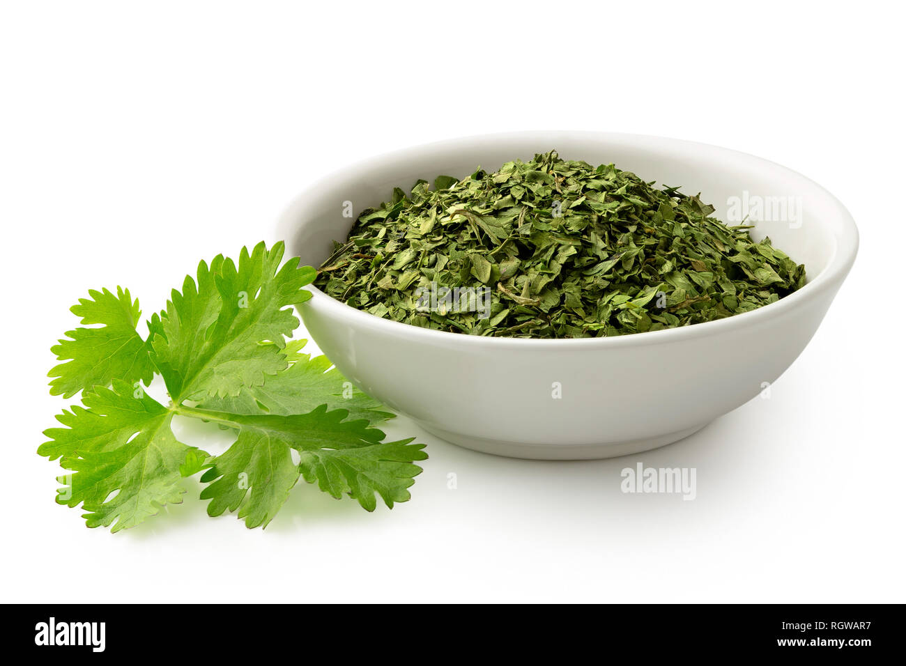 Dried chopped coriander leaves in white ceramic bowl next to fresh