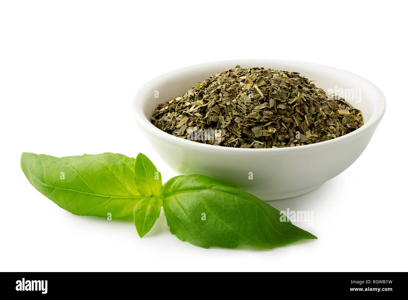 Dried chopped basil in white ceramic bowl next to fresh basil