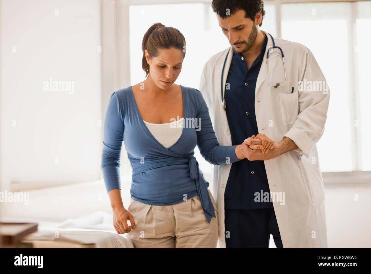 Male doctor assisting patient, holding her hand and helping her to walk