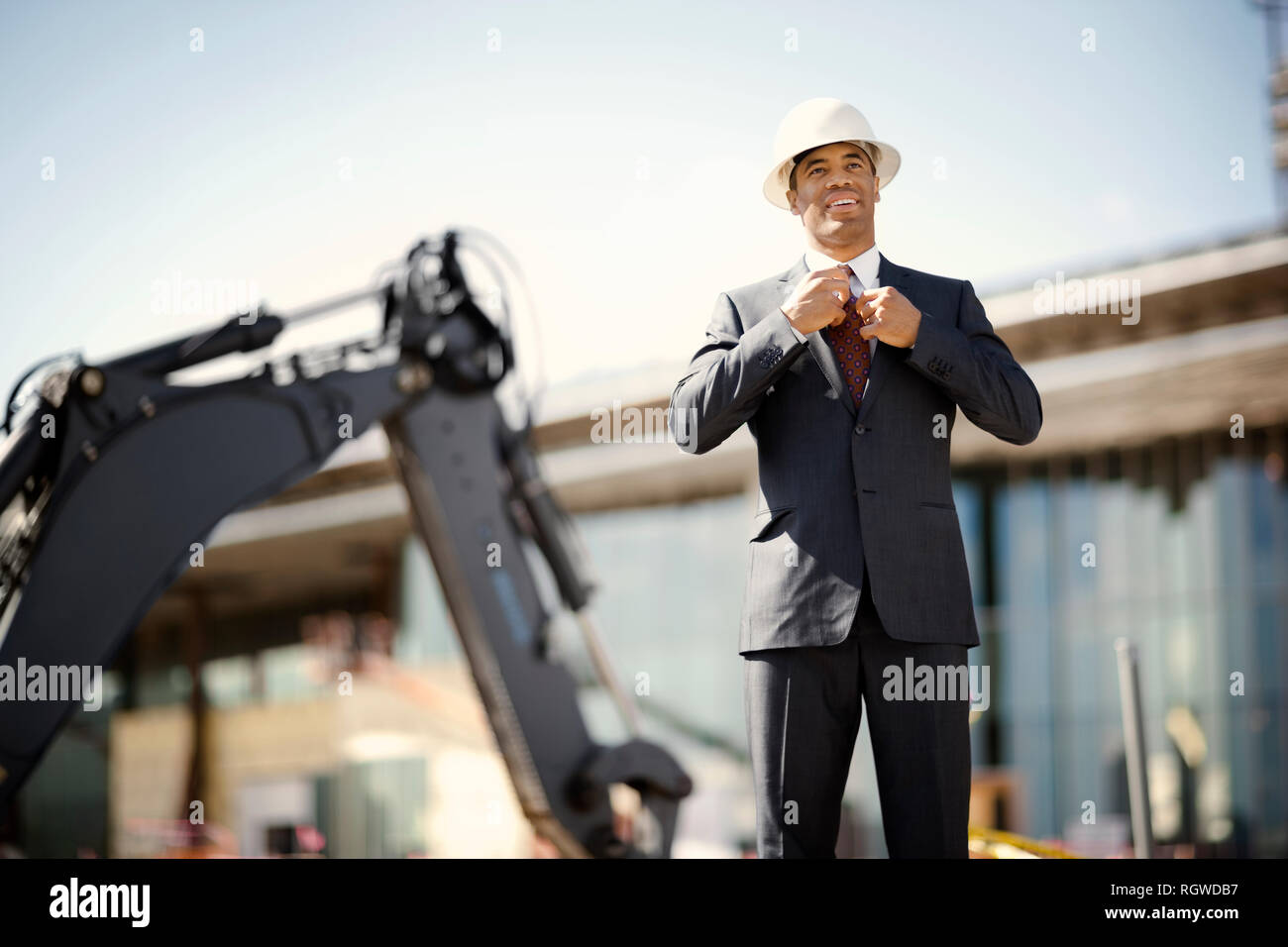 Young engineer wearing a suit and hardhat adjusts his tie while ...