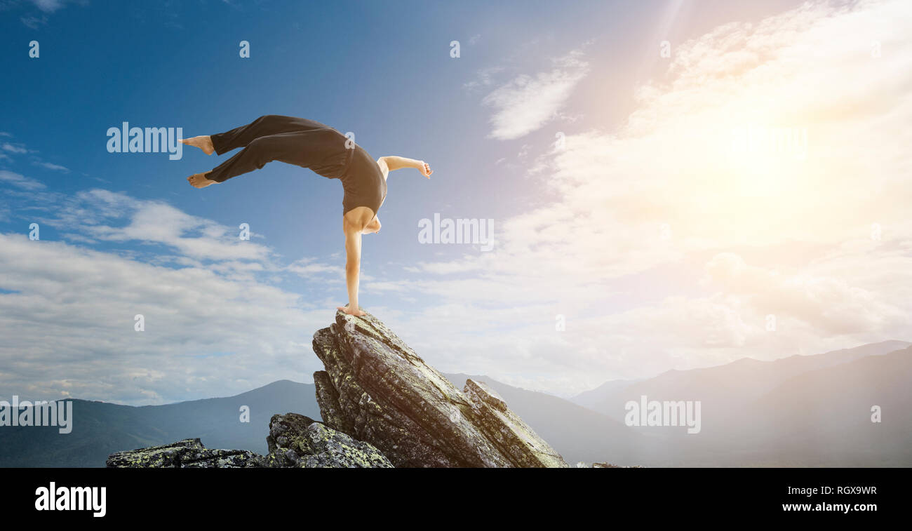 Amazing yoga man doing one handstand on rock edge. Mixed media Stock Photo