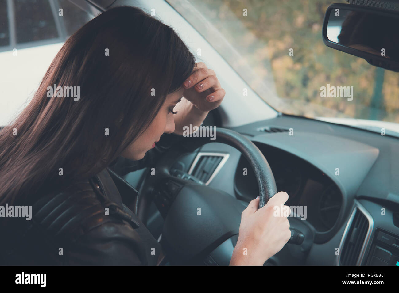 Closeup picture of young pretty lady waiting in car leaning on wheel with eyes closed on outdoors background. Girl feeling sleepy while waiting for so Stock Photo