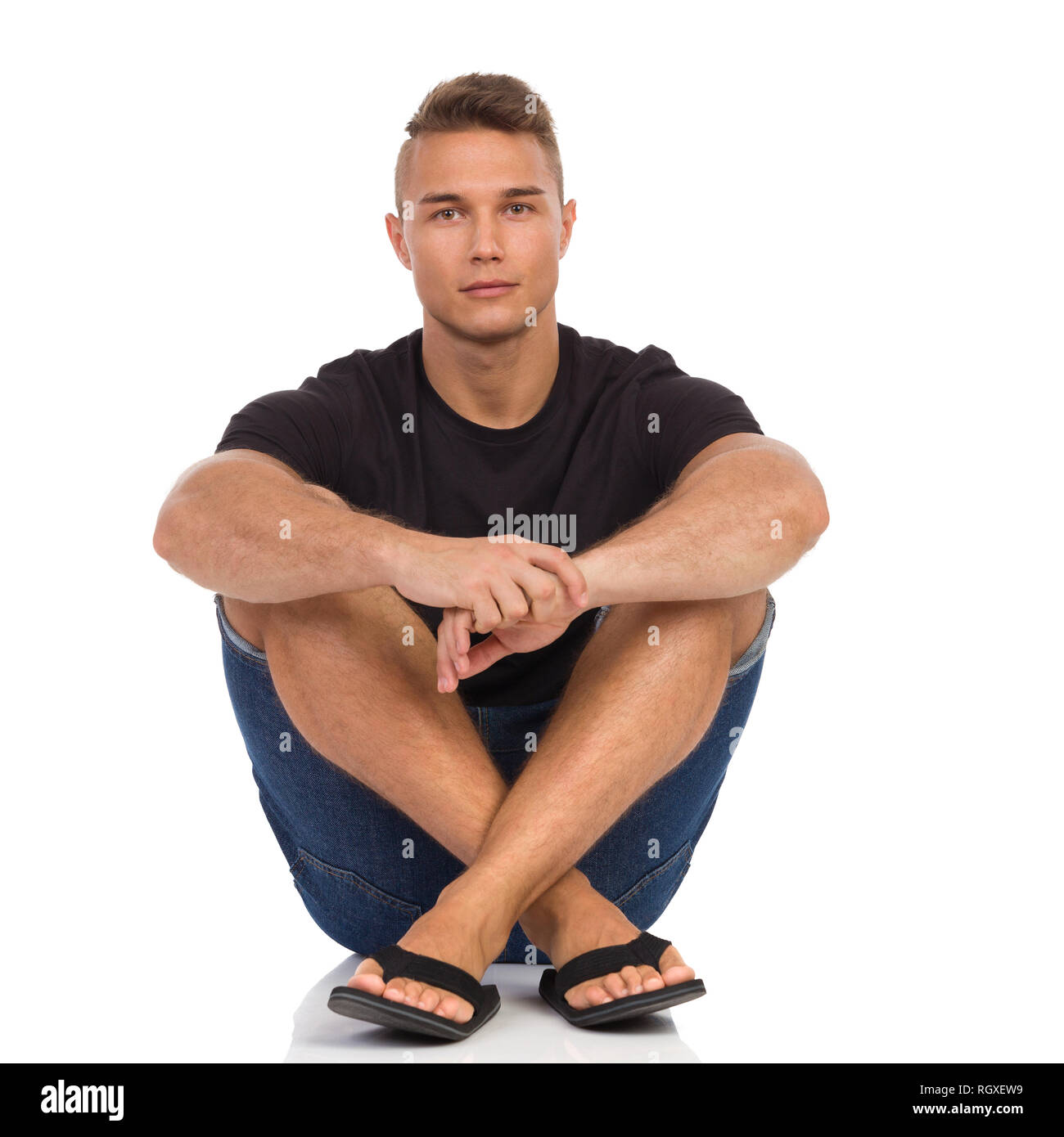 Young man in black shirt, jeans shorts and sandals, sitting relaxed on a  floor and looking at camera. Full length studio shot isolated on white  Stock Photo - Alamy