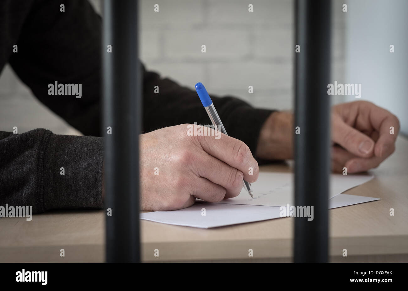 A prisoner behind bars writing a letter Stock Photo