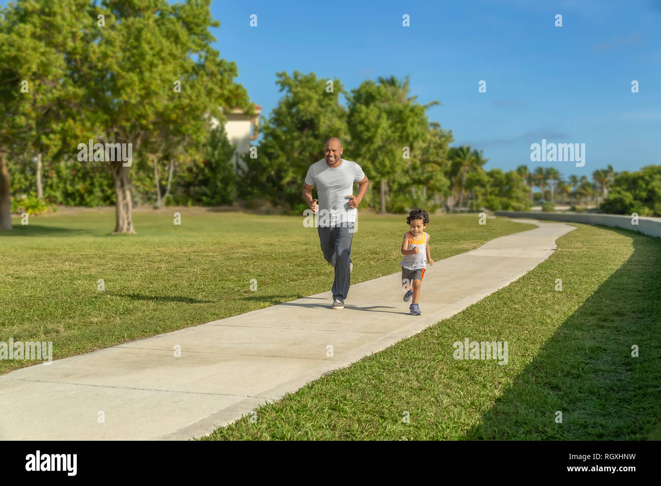 The son keeps up with his dad during a morning workout on a sunny day. The son keeps up with his dad during a morning workout on a sunny day. Stock Photo