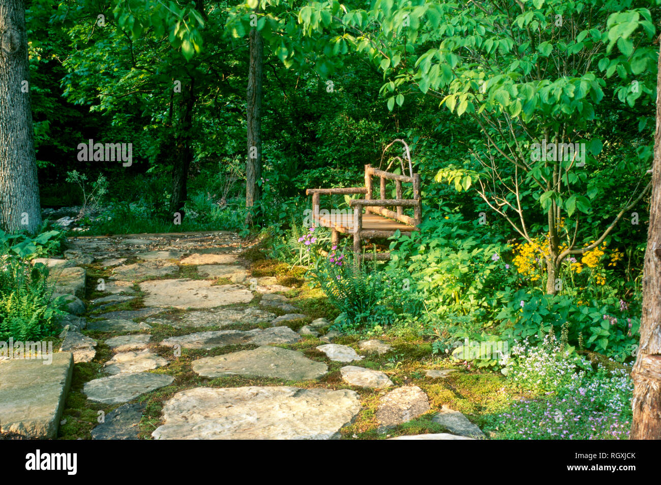Handmade bench on flagstone walkway in shade garden leading to creek