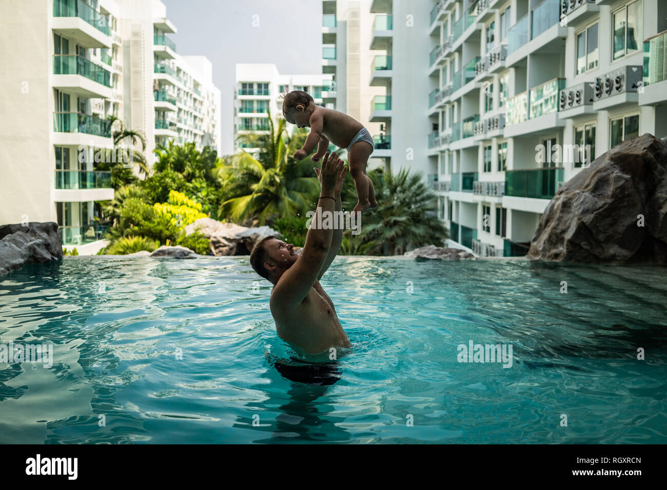 Dad throws baby in the pool on the background of coconut palms. Happy