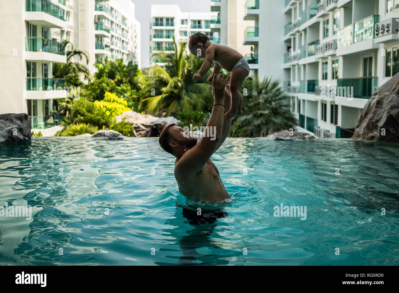 Dad throws baby in the pool on the background of coconut palms. Happy