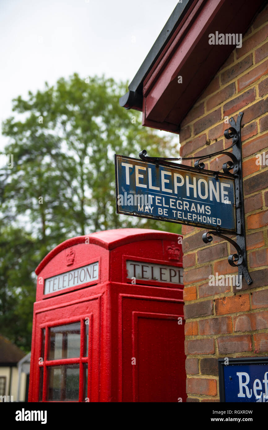 A quaint sign for a telephone and telegram on a wall, with a red telephone box behind it, at an old train station in Kent, UK. Stock Photo