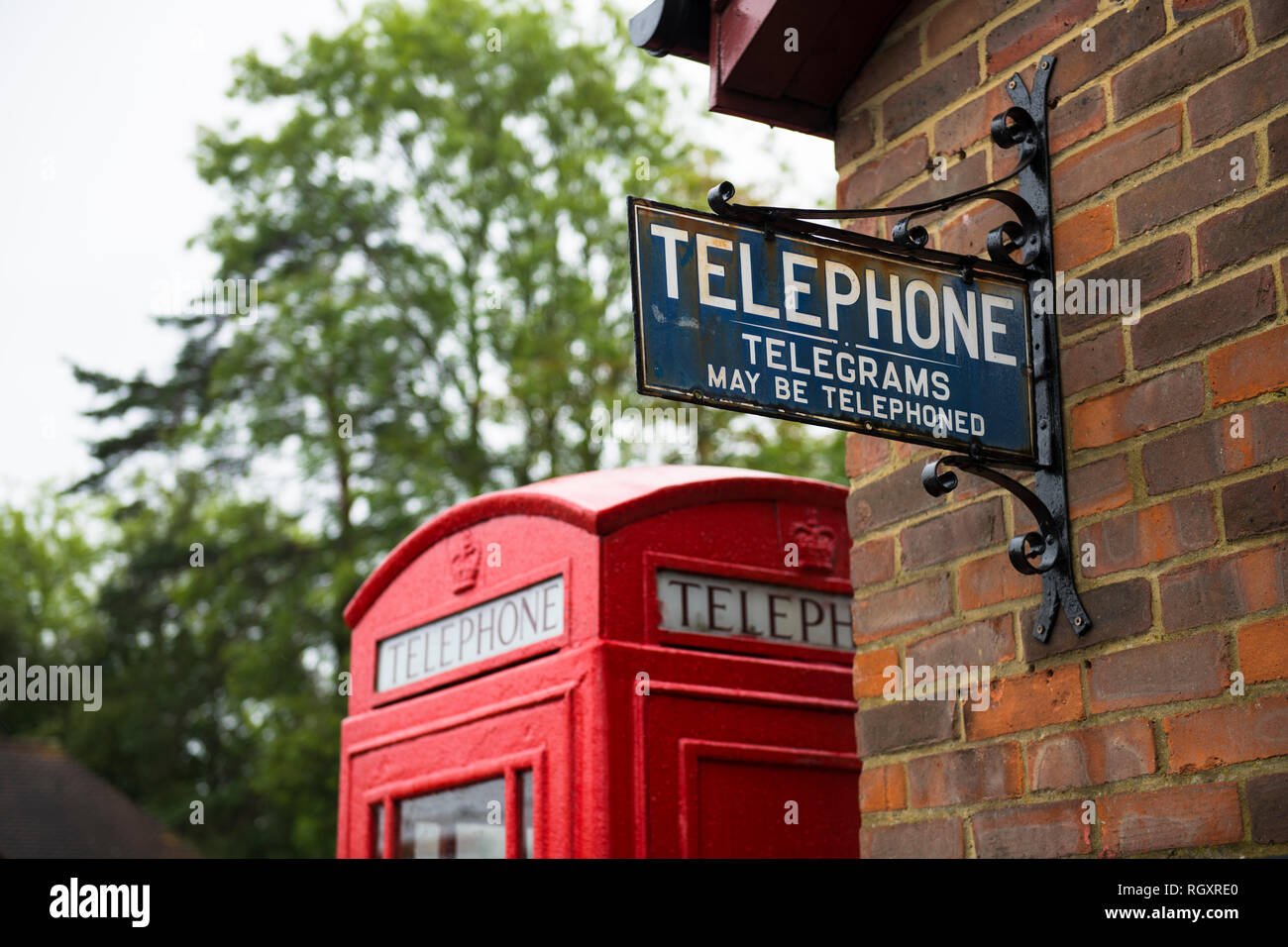 A quaint sign for a telephone and telegram on a wall, with a red telephone box behind it, at an old train station in Kent, UK. Stock Photo