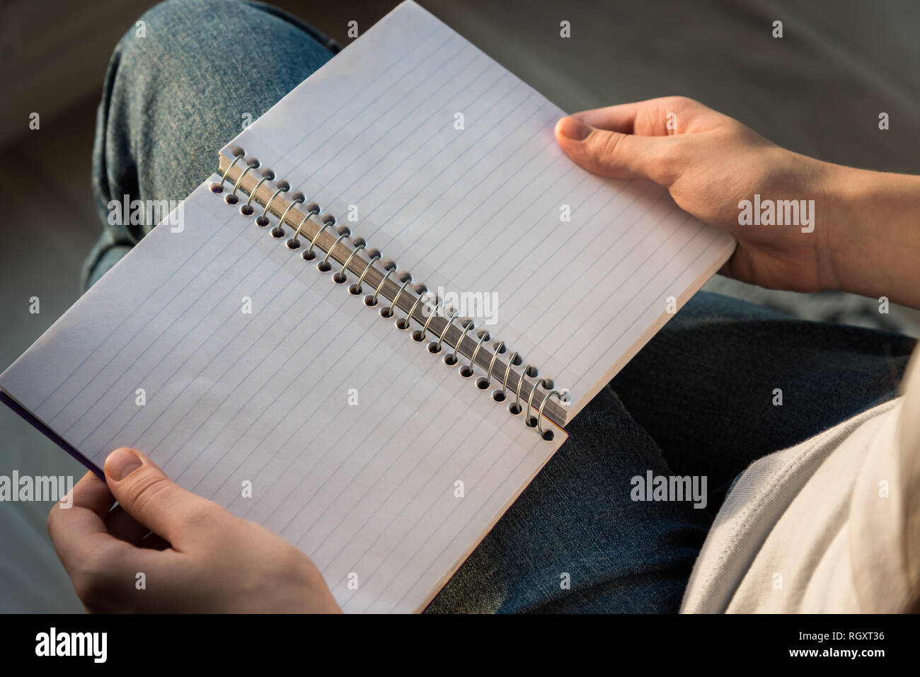 Woman holding spiral bound notebook with lined paper in lap, sitting in sunlight Stock Photo