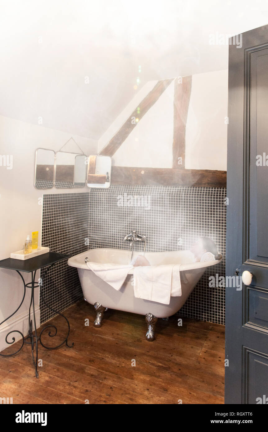 Woman relaxing in old fashioned steamy retro clawfoot bathtub. Wood