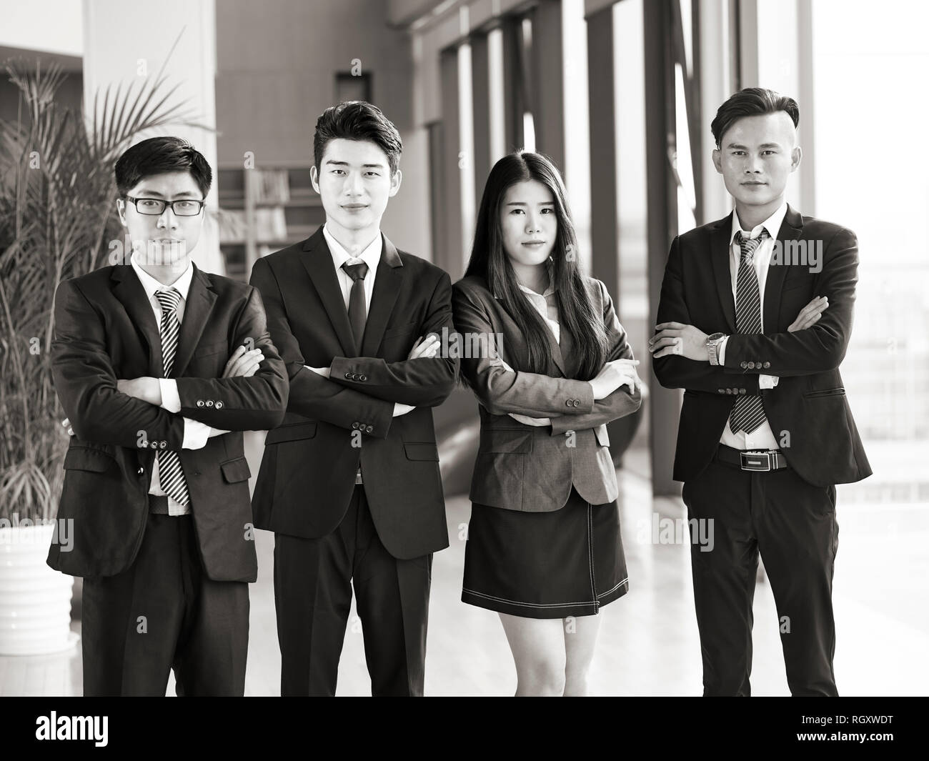 portrait of a group of young asian business people standing in office arms crossed, looking at camera, black and white. Stock Photo