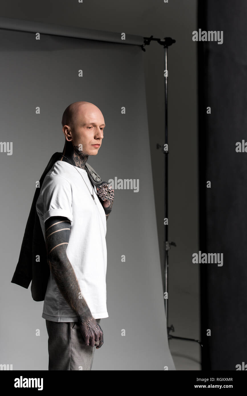 side view of handsome tattooed man holding suit jacket on shoulder and ...