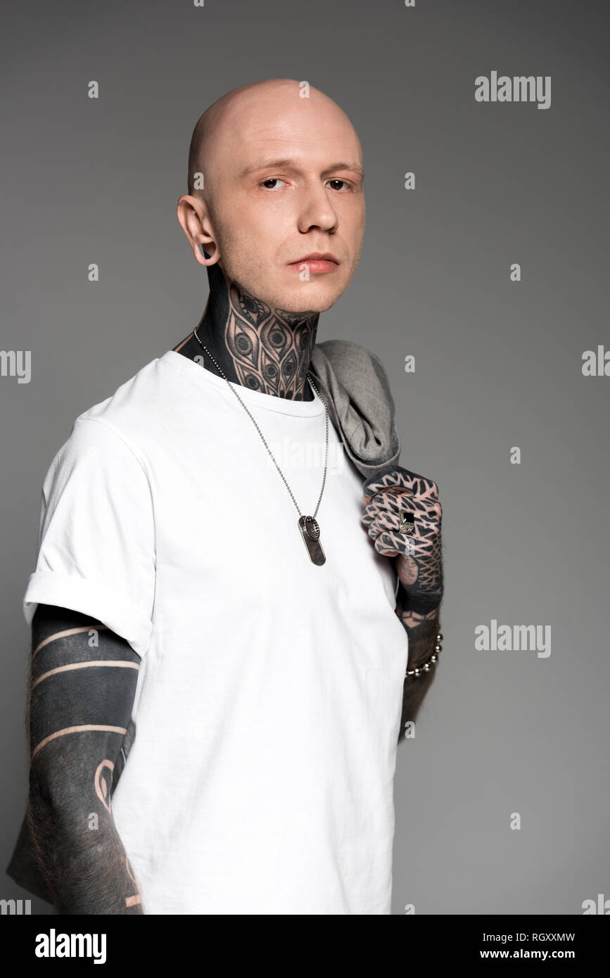 bald man with tattoos holding suit jacket on shoulder and looking at ...