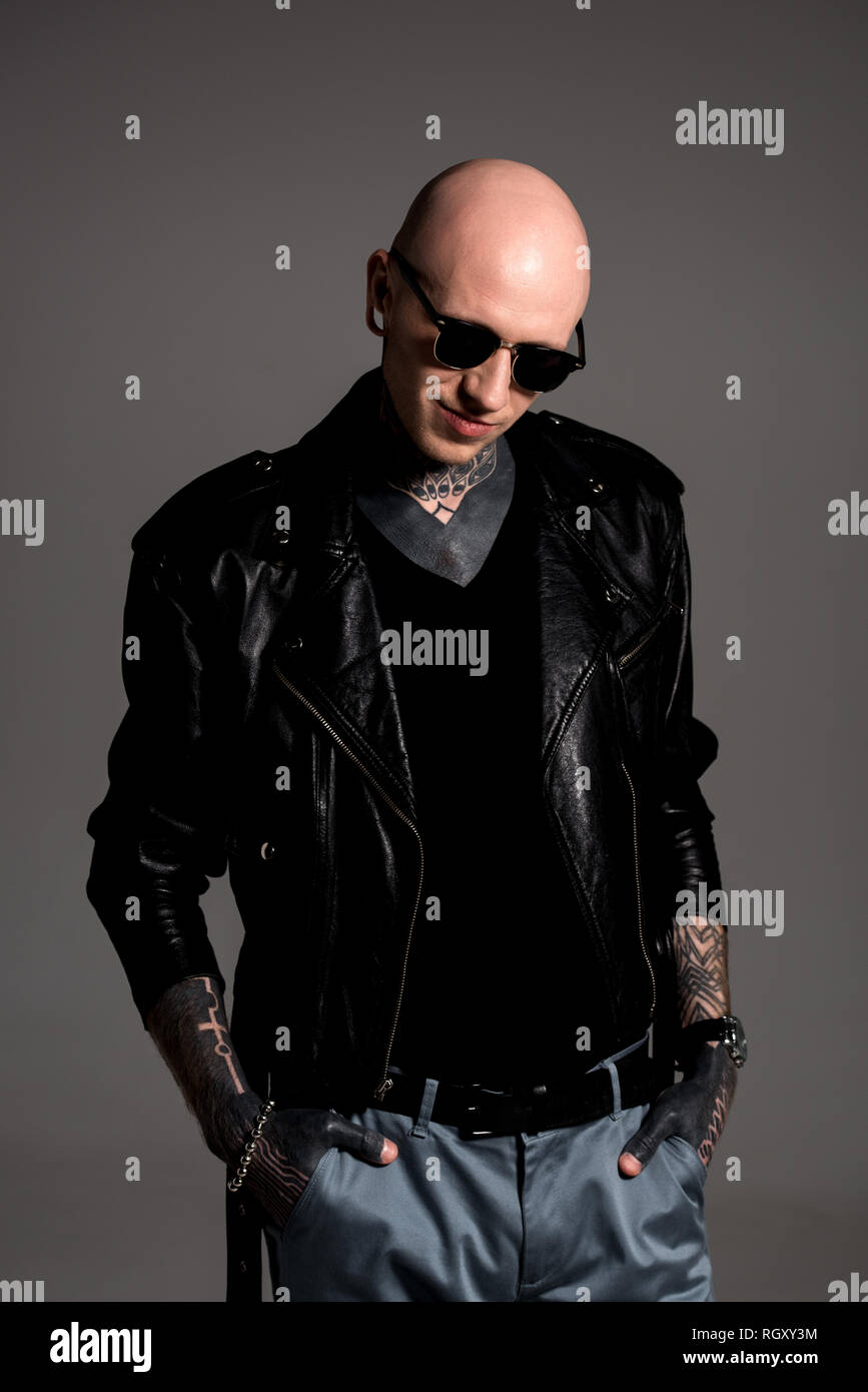 smiling bald tattooed man in leather jacket and sunglasses standing with  hands in pockets isolated on grey Stock Photo - Alamy