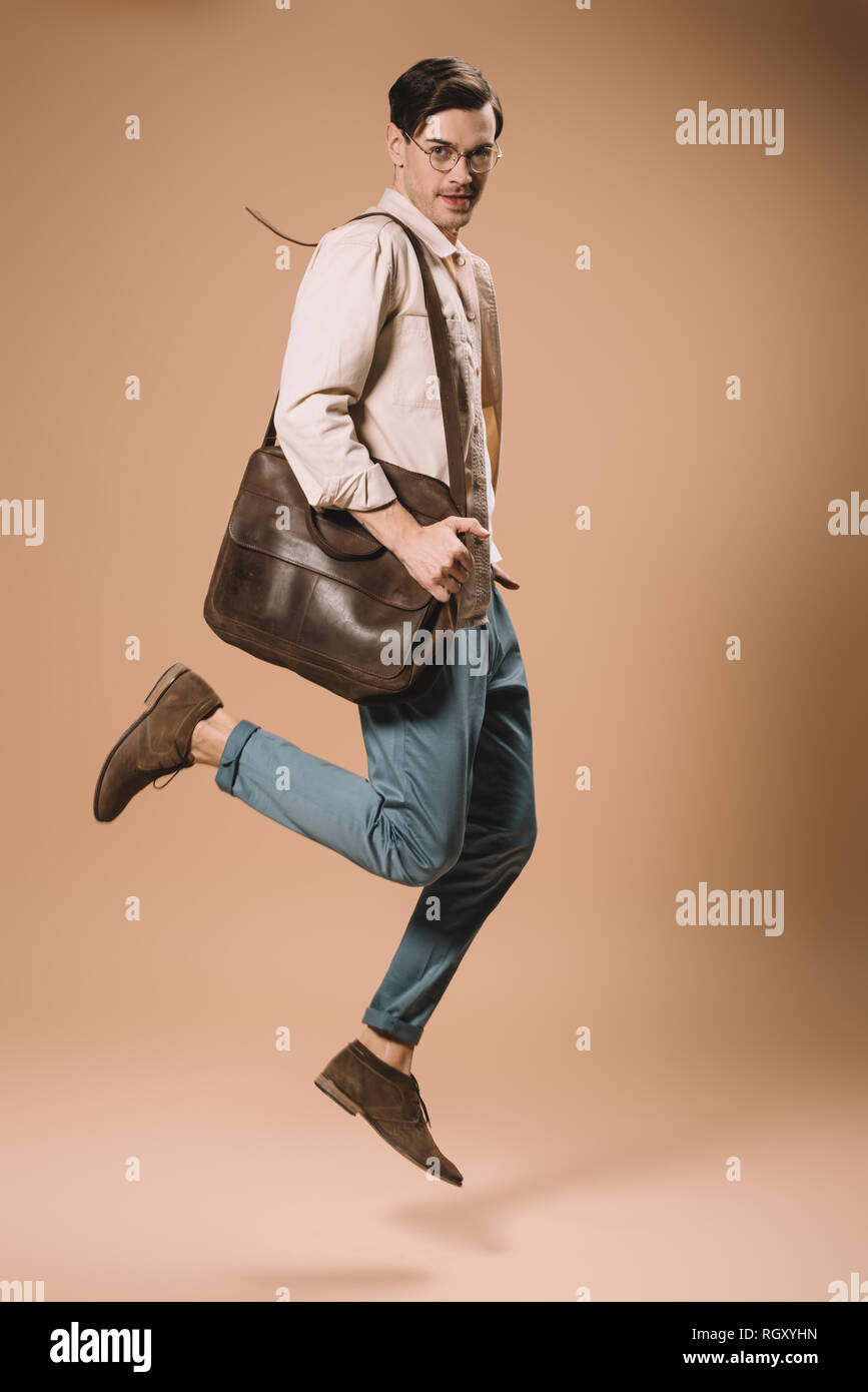 handsome man in glasses jumping with bag on beige background Stock Photo