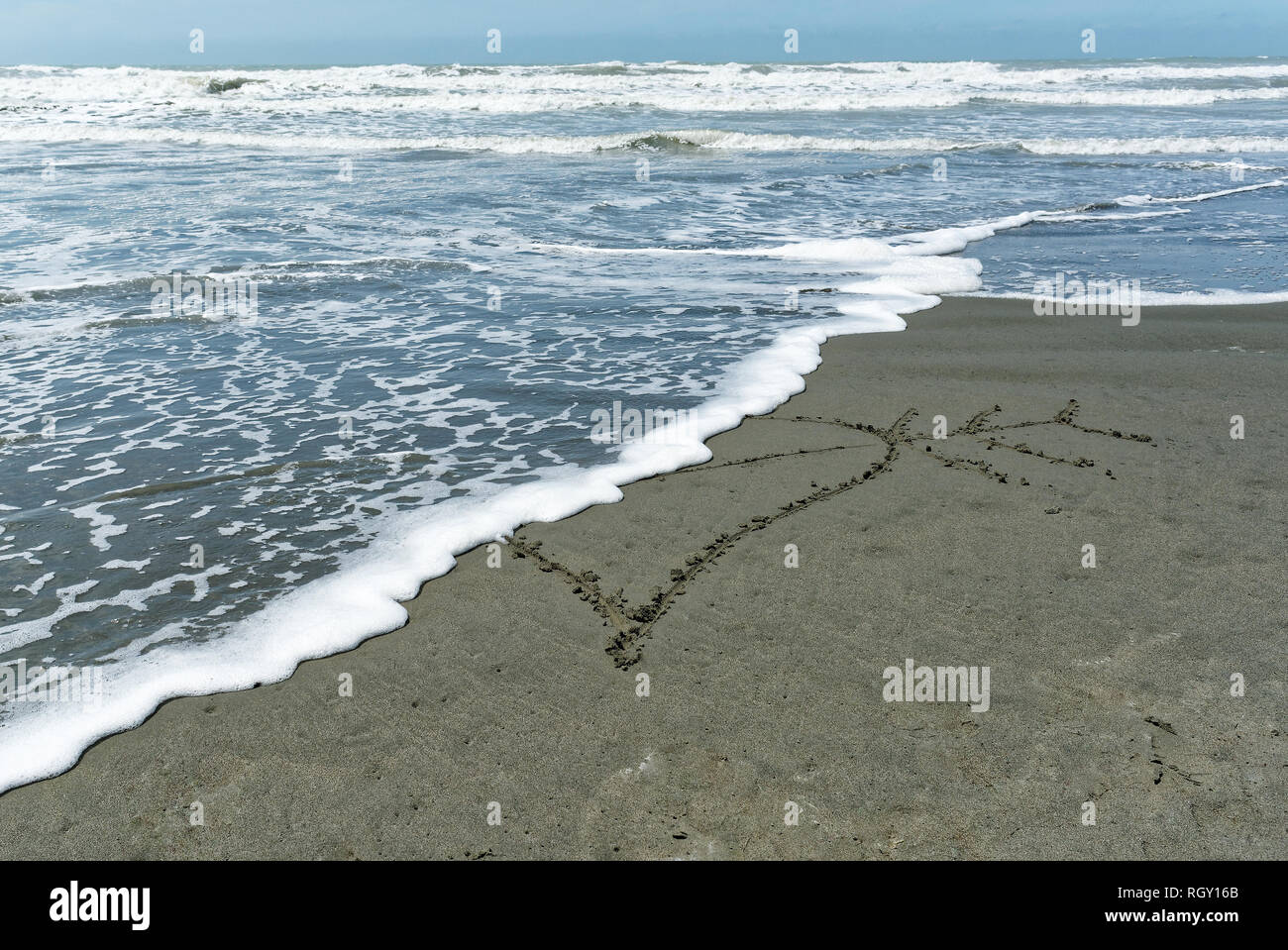 A heart drawn in the sand is cut in two by an incoming wave signifying lost love and being broken hearted Stock Photo