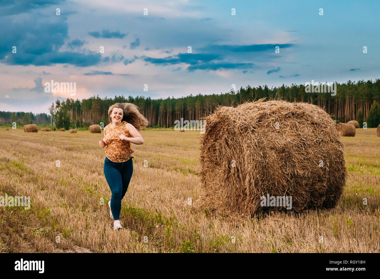 Beautiful Plus Size Young Woman Running Near Hay Bales In Summer Field Meadow At Blue Sly Background Stock Photo