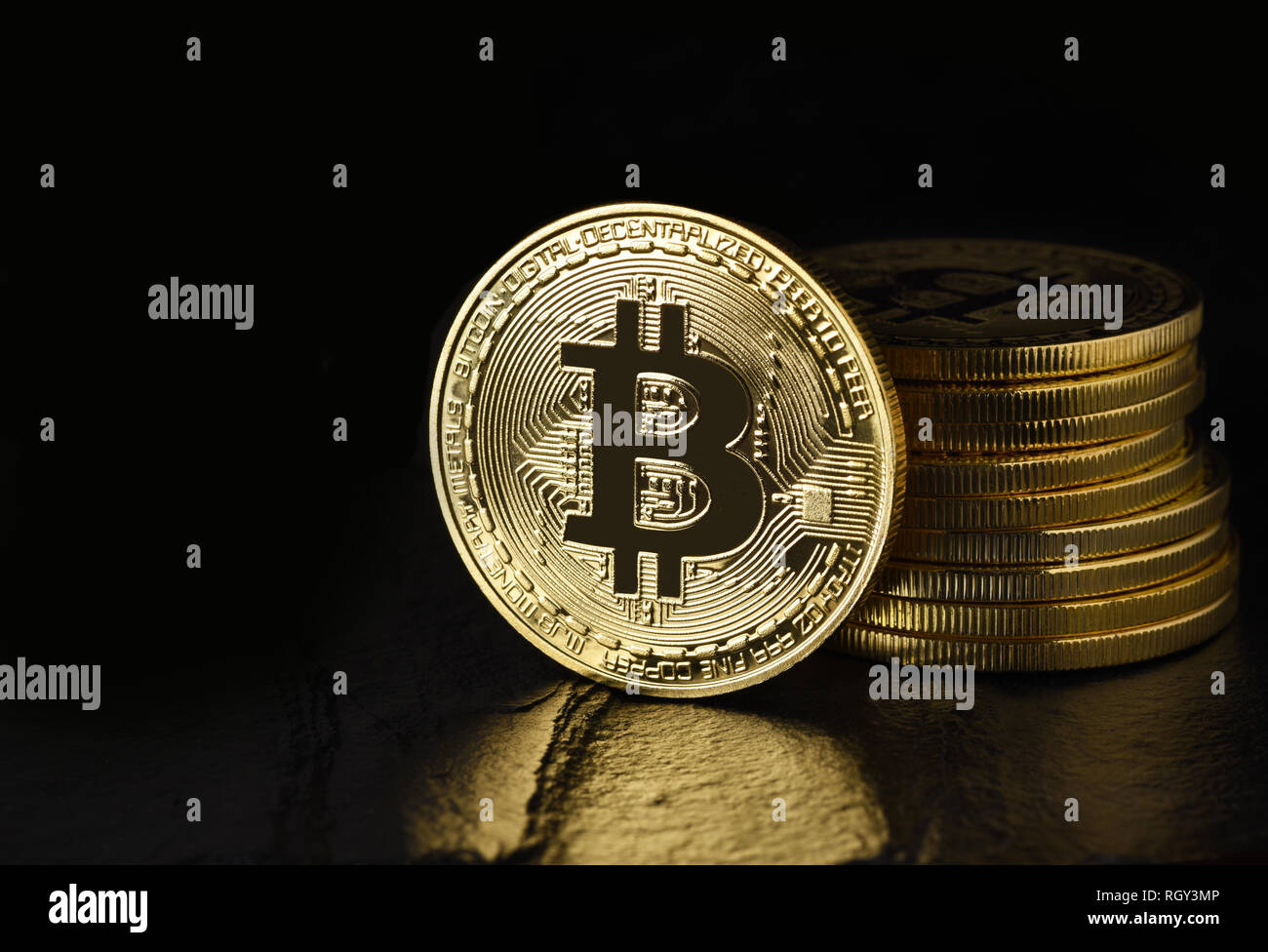 Bitcoin: Physical bit coin aslo called Digital Currency or Cryptocurrency, on edge standing in front of a stack, on black with reflection and copy spa Stock Photo