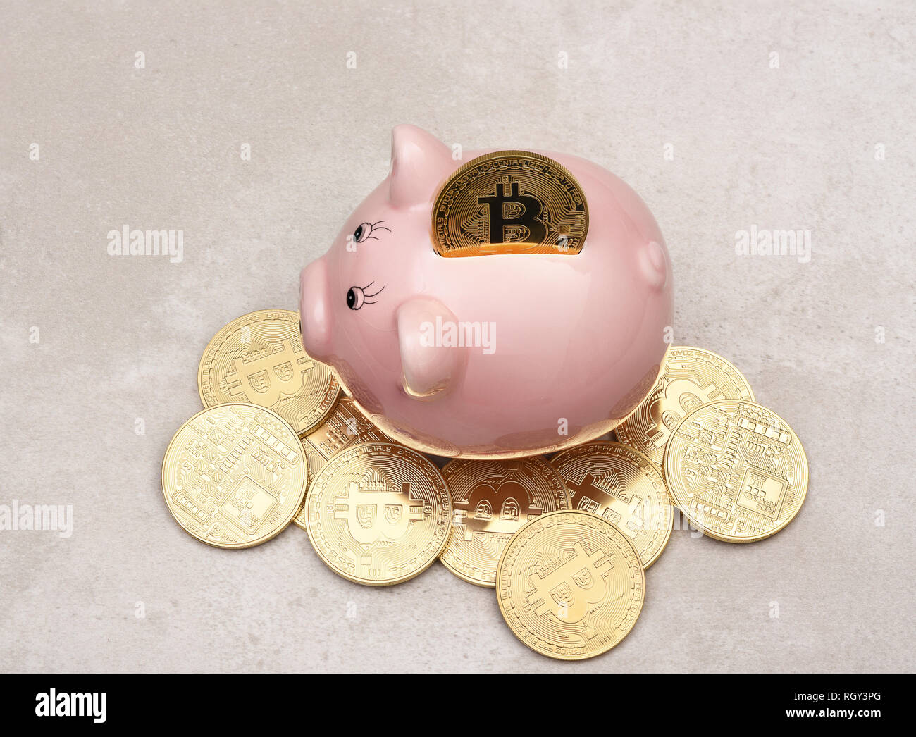 Savings Concept: A Bit Coin in the slot of a piggy bank with more coins on the table. Stock Photo
