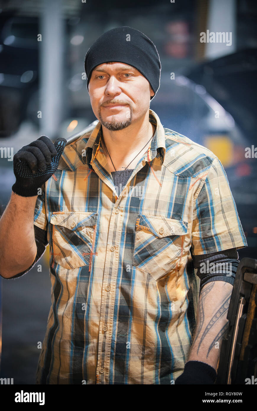 Car repair service. Brutal mechanic man in a black hat stands holding a