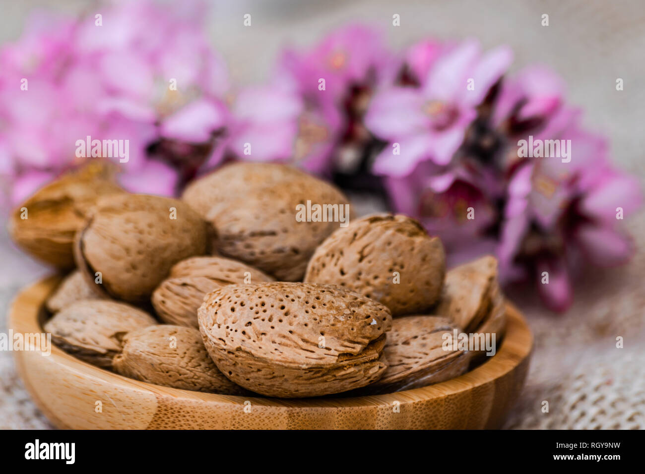 Almonds with shell in wooden bowl, with almond flowers blooming background Stock Photo