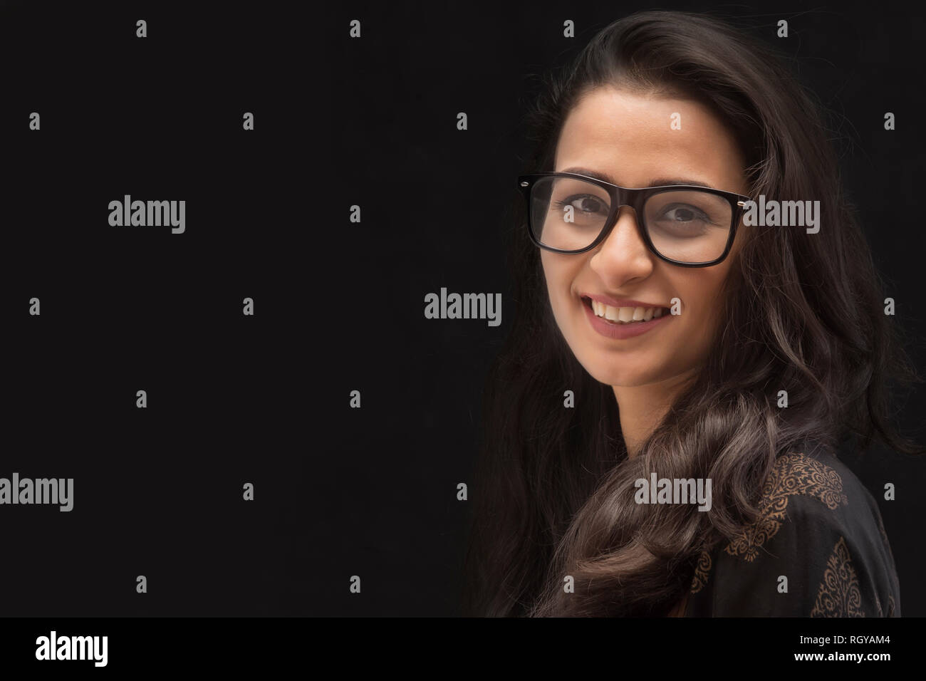 Portrait of a beautiful young woman smiling looking at camera wearing eyeglasses over black background Stock Photo