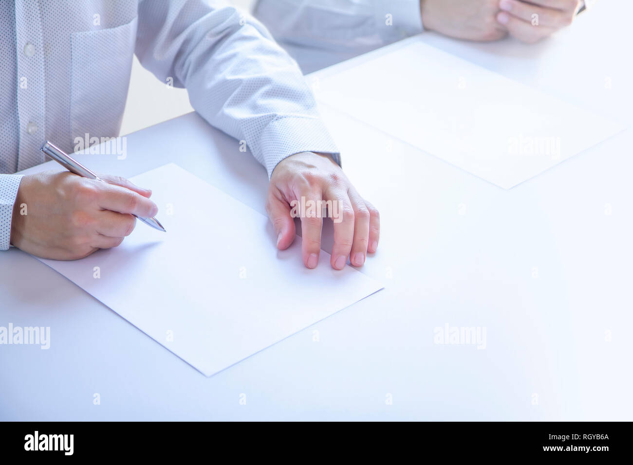 Businessmen in a meeting room partially cropped at their hands holding a pen with writing gesture on a plain blank white paper document as a blank moc Stock Photo