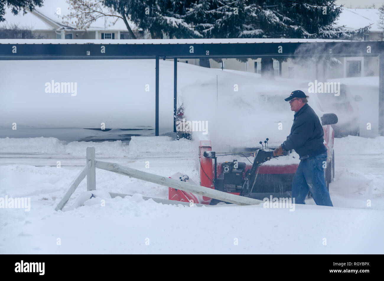 Extreme winter weather! A man clearing snow from a sidewalk with a mechanical snow blower after a winter storm in Michigan, USA. Stock Photo