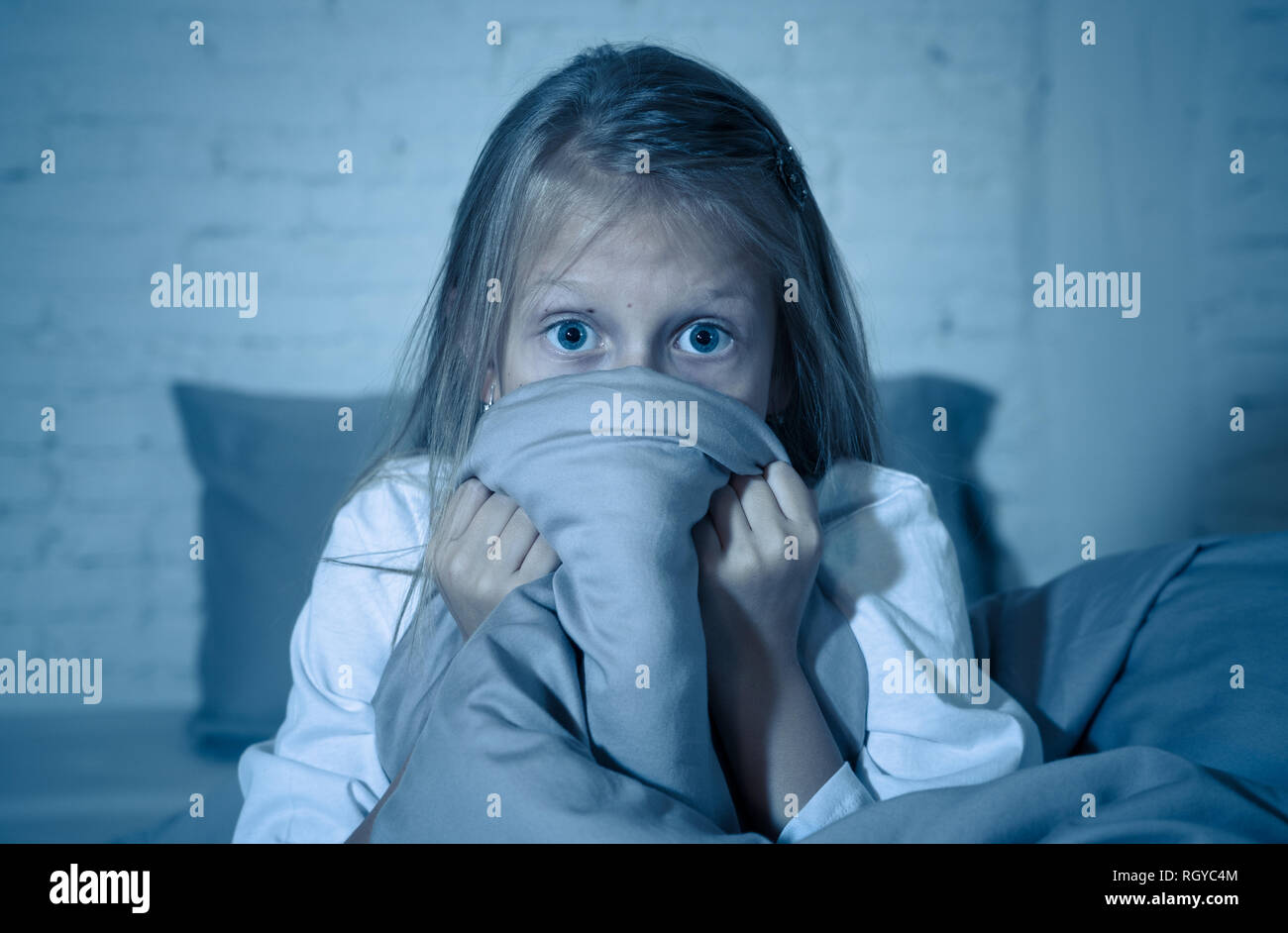 Scared little girl staying sleepless hiding behind the duvet looking