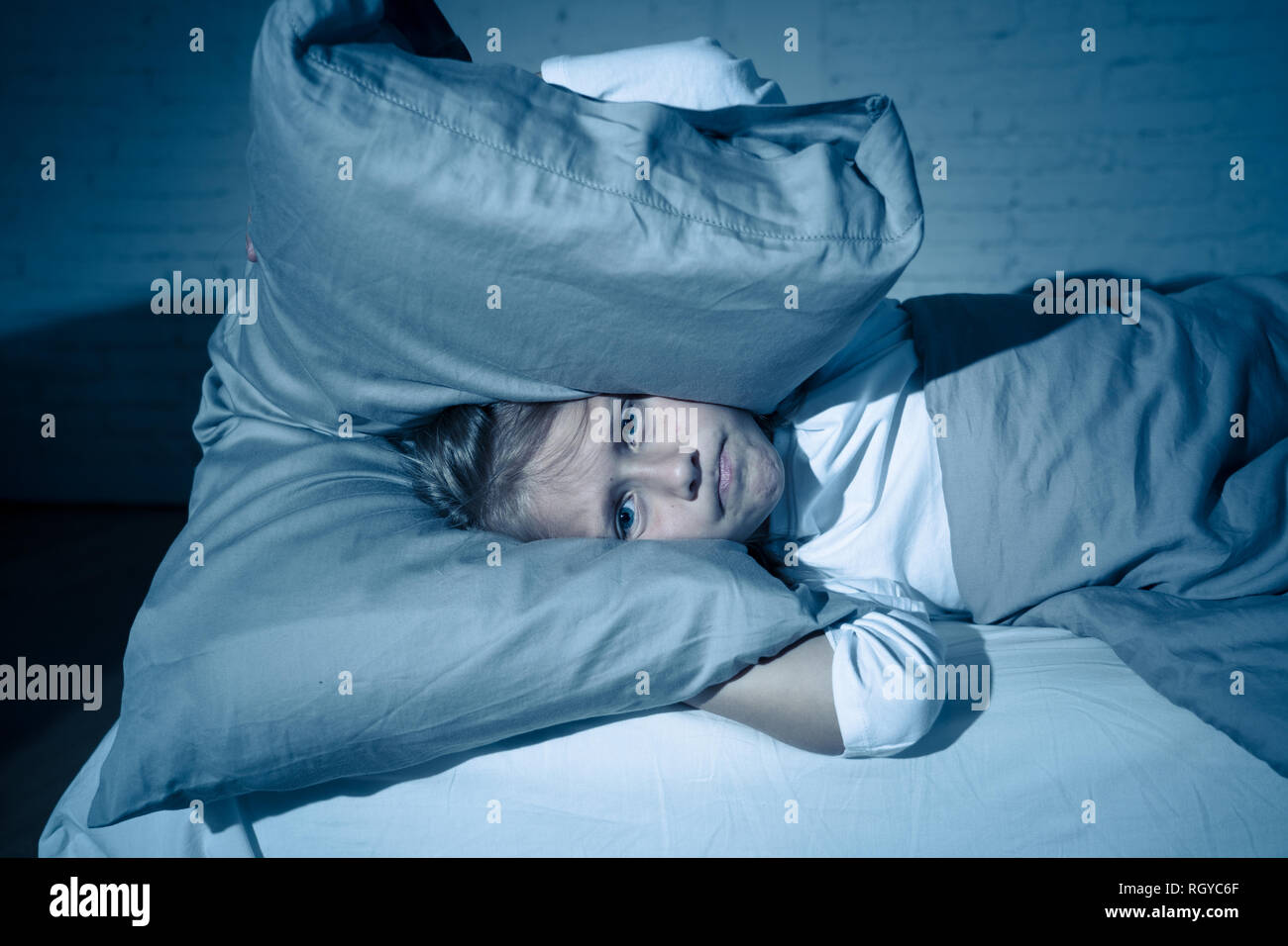 Unhappy girl covering her ears with pillow trying to sleep at night