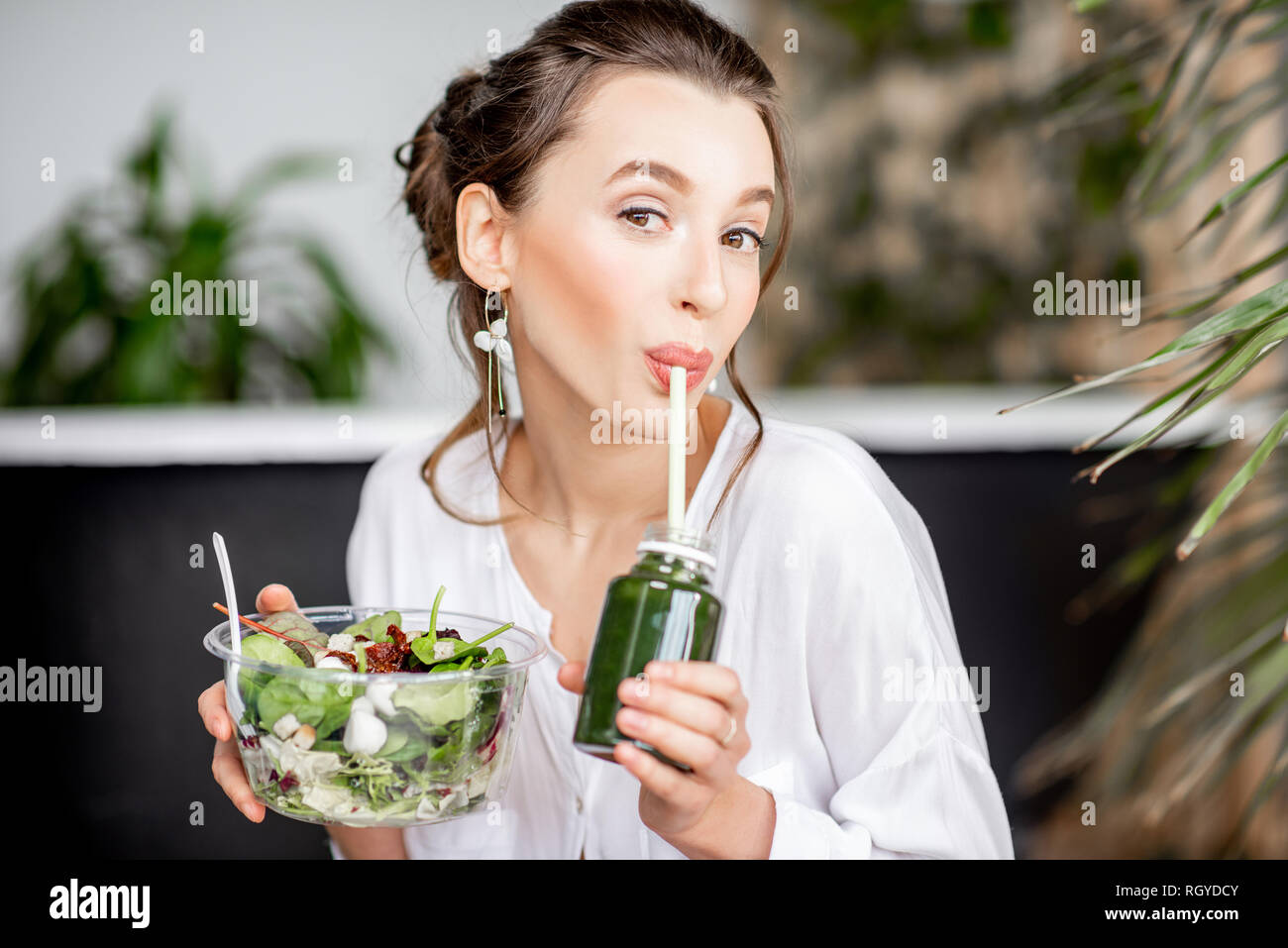 Beautiful woman drinking smoothie while sitting with healthy salad in the bathroom. Healthy eating and beauty concept Stock Photo